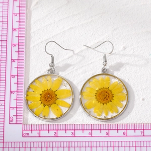 Macro shot of silver circular resin earrings with yellow dried daisies next to a ruler