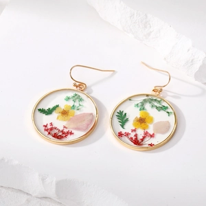 Pendientes de resina con flores secas en marco dorado sobre fondo blanco minimalista