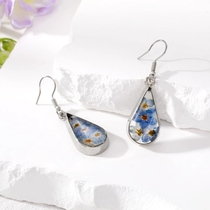 Detail of teardrop silver earrings with blue dried flowers on white stone background