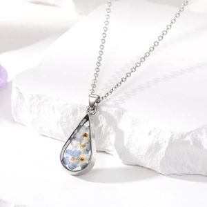 Close-up of a silver teardrop pendant necklace with preserved blue dried flowers