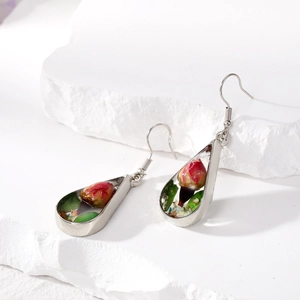 Detailed view of silver teardrop earrings with real red dried rose buds and green leaves