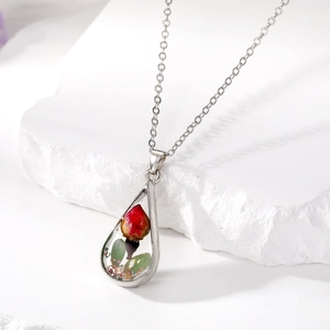 Macro detail of teardrop necklace pendant featuring real dried red flowers and green leaves