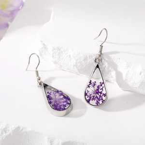 Detail view of teardrop earrings with purple dried flowers in resin on white stone