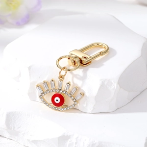 Golden Evil Eye keychain with red crystal and hollow diamond eyelashes on a stone stand