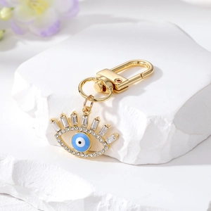 Golden Evil Eye keychain with blue enamel and sparkling crystals on white marble