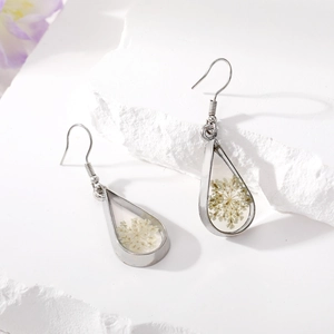 Detail of drop-shaped earrings featuring white dried flowers in silver metal frame