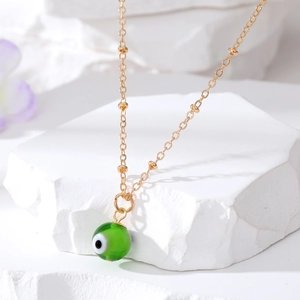 Close-up of golden necklace with green Evil Eye bead pendant on white stone