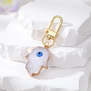 Hamsa hand evil eye keychain with gold trim on white stone display for accessories