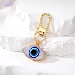 Detail of white druzy evil eye keychain with gold trim on a white stone background