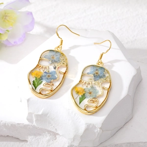 Vue détaillée de boucles d'oreilles visage avec de vraies fleurs séchées dans la résine