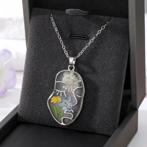 Pendentif visage abstrait avec de vraies fleurs séchées en résine transparente