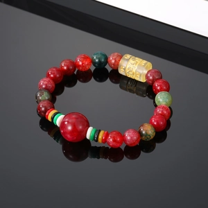 Macro shot of red agate beads with a yellow cylinder bead featuring etched Sanskrit symbols