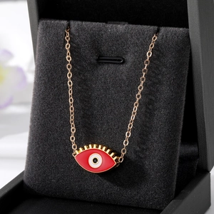 Détail macro du pendentif œil porte-bonheur en émail rouge avec cils dorés sur fond noir