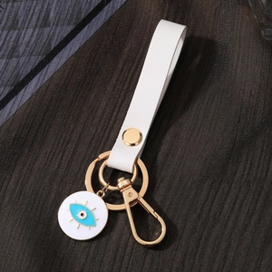 Geometric evil eye keychain with white leather strap and gold ring on grey fabric