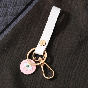 Detail of the white leather strap and evil eye enamel charm on a golden keychain