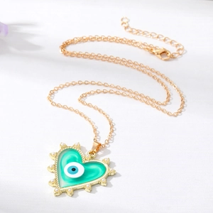 Collier cœur doré avec émail vert, œil protecteur et perles sur un fond blanc texturé