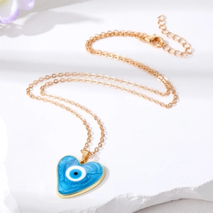 Golden heart necklace with blue Evil Eye resin pendant on a white stone background