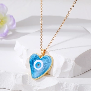 Detail of gold heart pendant with blue marble evil eye resin on stone background