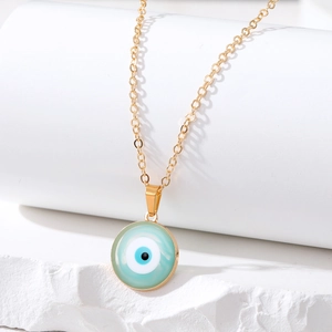 Close-up of golden evil eye necklace with mint green enamel charm on white stone blocks