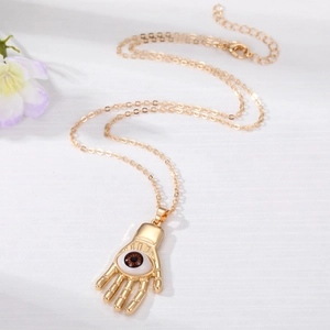Collier bohème doré avec pendentif main de Fatma et œil maléfique sur fond blanc texturé