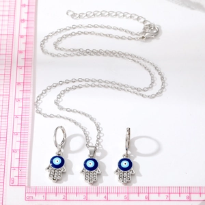 Hamsa hand and evil eye jewelry set with blue enamel and crystals on white background