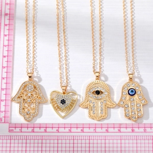 Bohemian gold Hamsa and heart pendants with evil eye rhinestones shown with measurement ruler