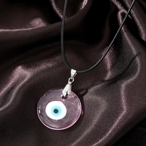 Macro shot of pink resin Evil Eye pendant with black wax cord on silk background
