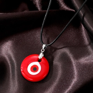 Detail of red evil eye glass pendant with black cord on brown silk fabric