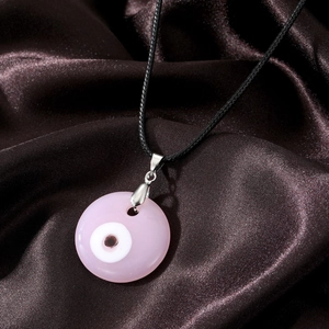 Close-up of a pink resin Evil Eye pendant with a black cord on brown silk fabric