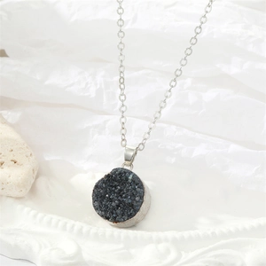 Detail van een zilverkleurige ketting met ronde hanger en donkerblauwe kristallen stenen