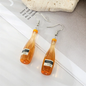 Détail de la boucle d'oreille bouteille de vin en résine orange sur une pierre blanche