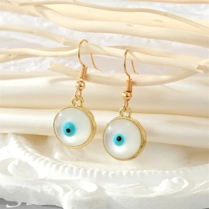 Detailed close-up of golden evil eye drop earrings hanging on a white wooden branch