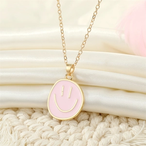 Macro shot of pink enamel smiley face pendant on a golden chain against white fabric