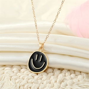 Golden chain necklace with black enamel smiley face pendant on white satin background