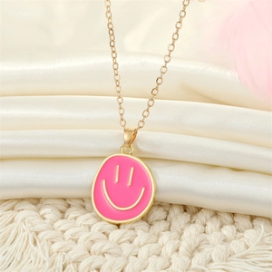 Close-up of pink enamel smiley face pendant with gold alloy chain on white silk