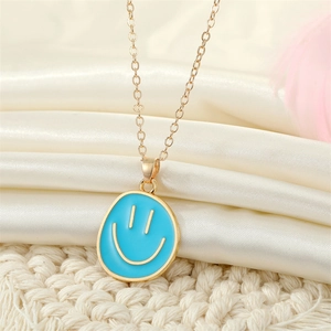 Close-up of golden necklace with light blue smile face pendant on silk fabric