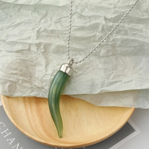 Détail du pendentif piment en résine verte avec chaîne à billes sur plateau en bois