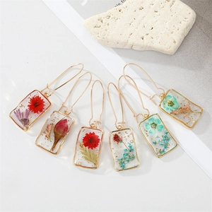 Detailed macro of rectangular resin earrings with colorful dried flowers and gold leaf