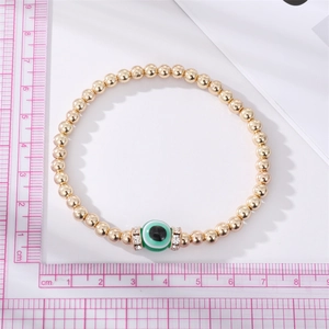 Close-up of handmade beaded bracelet featuring green evil eye bead and gold beads