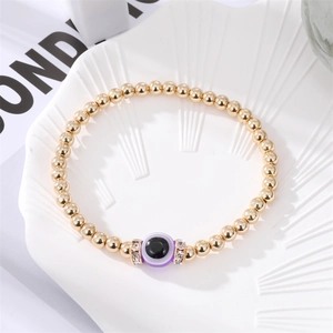 Golden beaded evil eye bracelet with purple charm and crystal spacers on a white shell tray