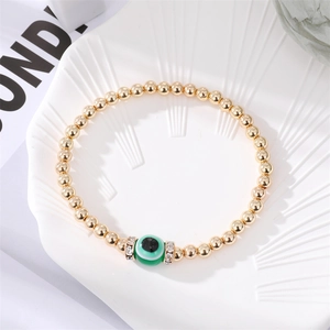 Detailed close-up of a golden beaded Evil Eye bracelet with green crystal accents and rhinestones