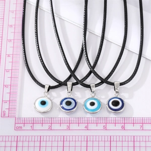 Nahaufnahme von vier Evil Eye Anhängern mit schwarzer Kordel auf einer Messskala