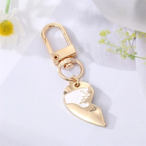 Detail of a golden heart gesture keychain with white enamel on a clean floral background