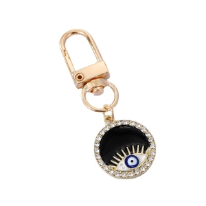 Golden Evil Eye keychain with black enamel, eyelashes and crystal accents on white background