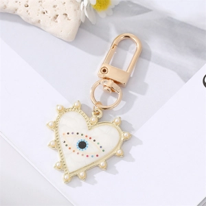 Dettaglio portachiavi a cuore con occhio del male, smalto bianco e bordo di perle