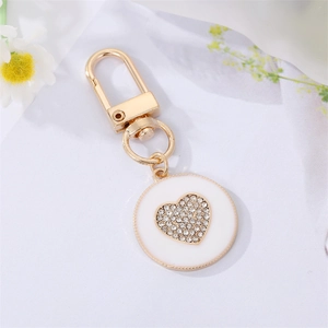 Close-up of golden alloy keychain featuring white enamel round pendant with zircon heart inlay
