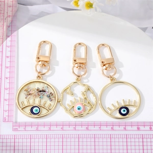 Trois porte-clés œil grec en alliage doré avec perles bleues sur un tapis de mesure