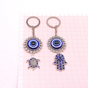 Macro view of evil eye turtle and hamsa hand keychains with blue rhinestones