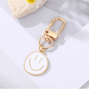 Detail of a gold-plated smiley face keychain with a D-ring clasp on a white background