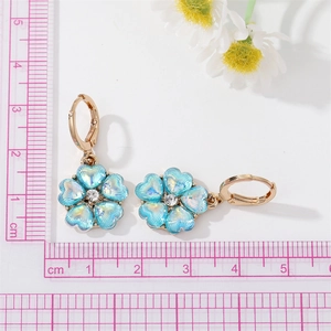Détail de boucles d'oreilles fleur, pétales bleu cœur et zircon près d'une règle
